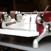 This image is a front-side view of the Slayer Espresso custom machine, leather sides, back/front panel and drip/cup trays powder coated white, x-legs powder coated silver, peruvian walnut wood accents, 2 groups at traditional height, manual dosing. 